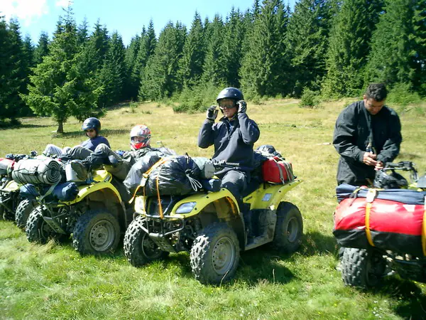 Tabărăși cu căști pregătindu-se de plecare pe ATV-uri, într-o poiană de munte