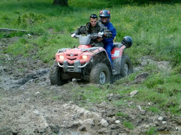 Doi participanți pe un ATV roșu trecând prin noroi pe un traseu înierbat