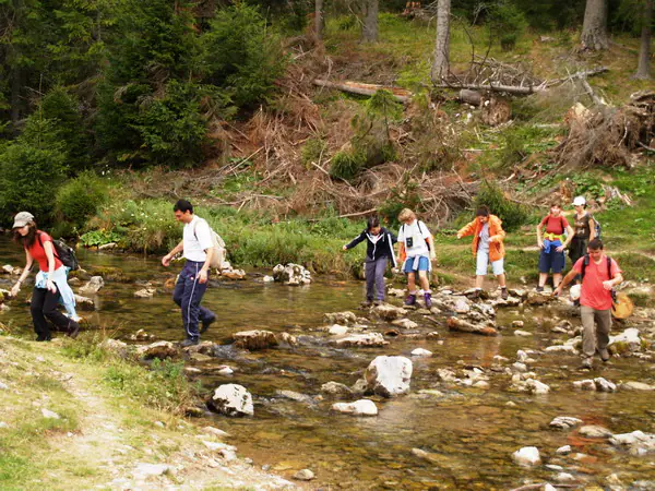 Grup de tabărăși traversând un pârâu de munte pe pietre