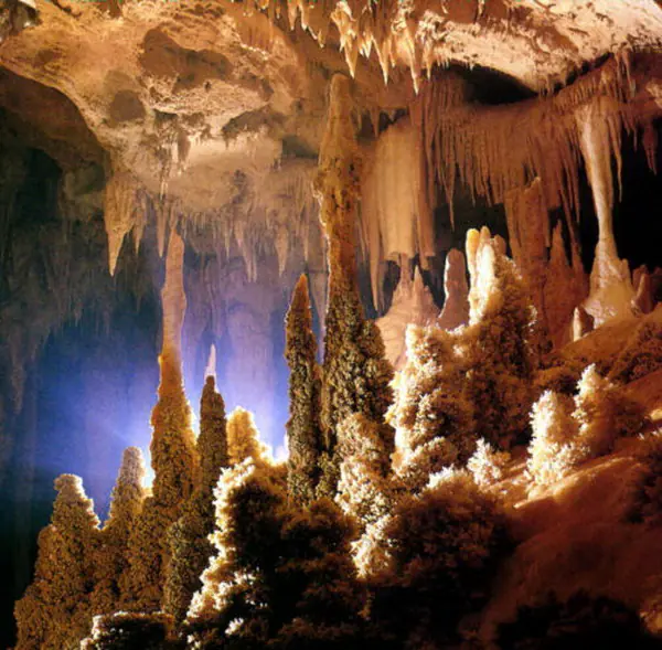Sală de peșteră plină de stalactite și stalagmite, în lumină caldă