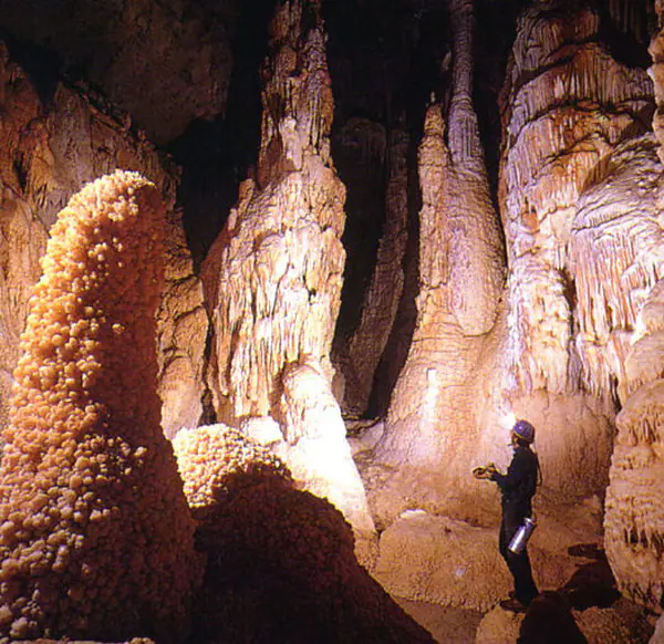 Speolog mic în fața unor coloane uriașe de stalagmite, într-o sală mare