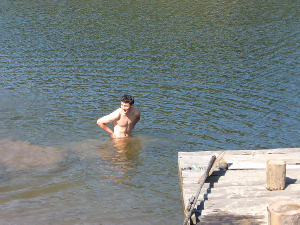 Tânăr înotând în lac lângă un ponton din lemn