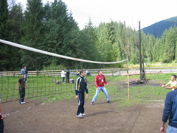 Jucători la fileul de volei pe terenul de sport al taberei, lângă pădure