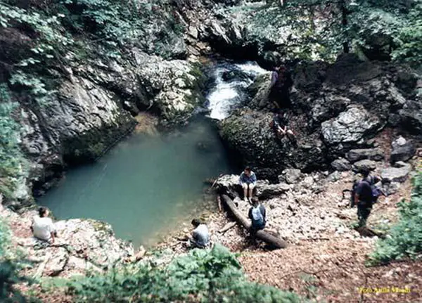Drumeți în jurul unui lac turcoaz sub o cascadă, într-una dintre dolinele Ponorului