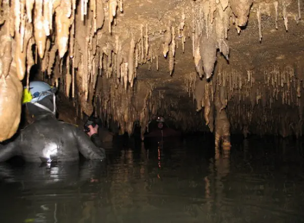 Speolog traversând prin apă un lac subteran, sub un tavan de stalactite