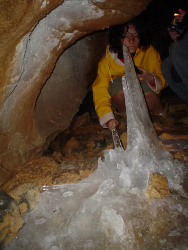 Explorator ghemuit lângă o stalagmită mare de gheață în Peștera Zmeilor (Onceasa)