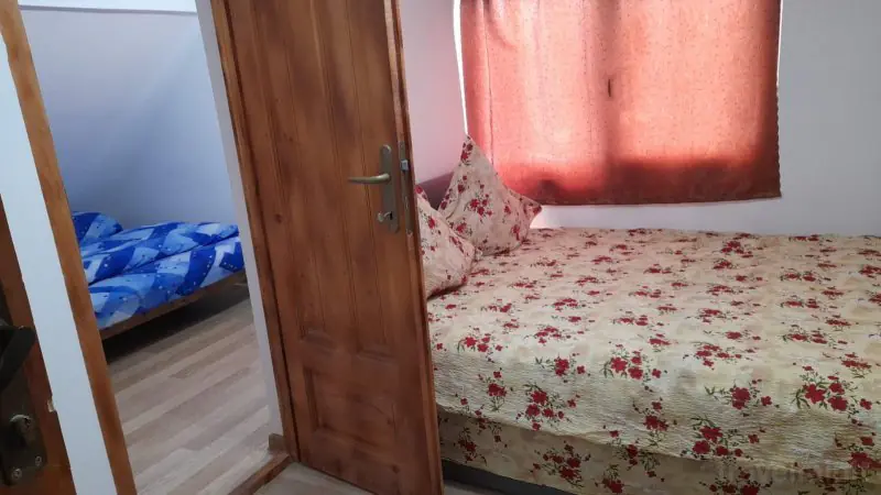 Pat dublu cu lenjerie cu flori văzut prin ușa deschisă, cu un pat single în camera alăturată