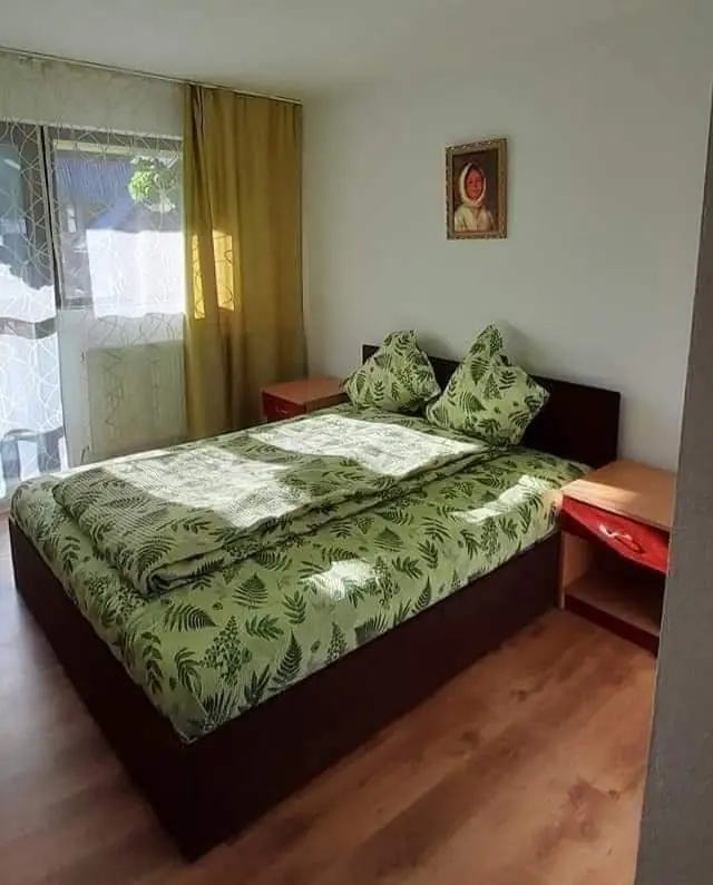 Cameră dublă însorită cu lenjerie verde cu frunze și noptiere roșii
