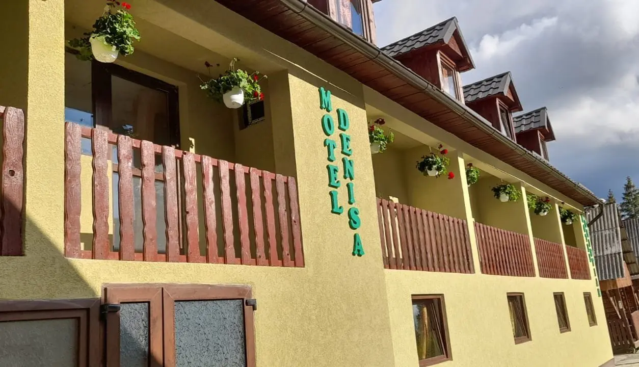 Fațada galbenă a Motelului Cristian & Denisa cu balustrade din lemn și ghivece cu flori