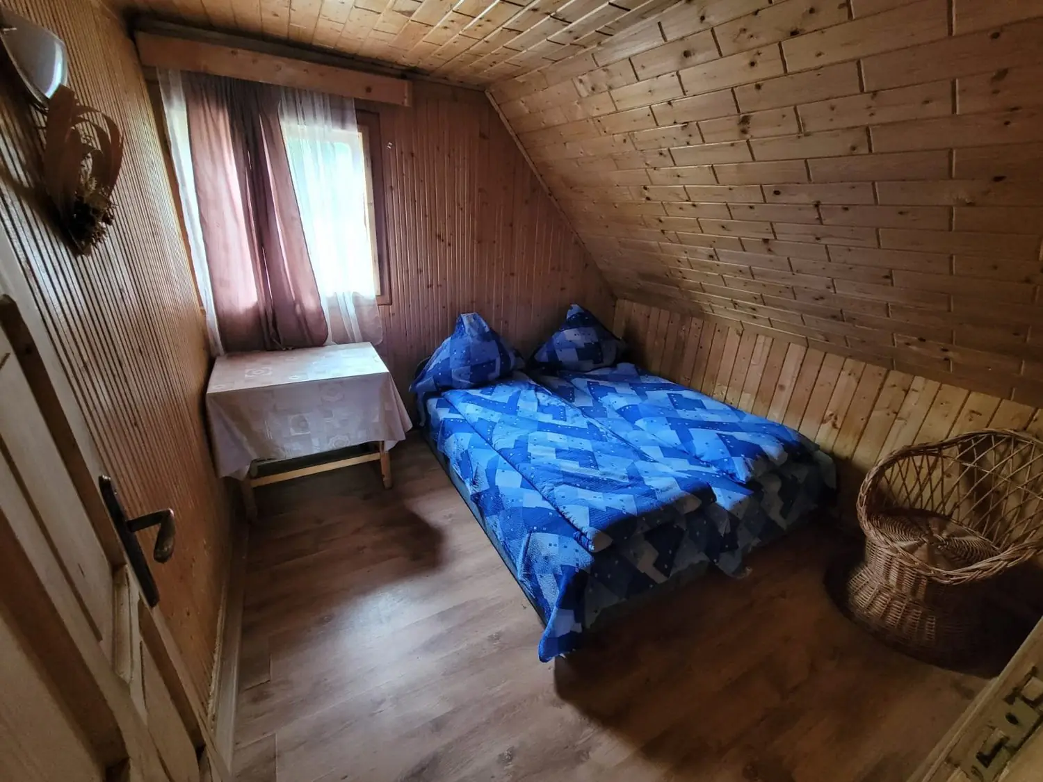 Dormitor la mansardă îmbrăcat în lambriu, cu pat cu lenjerie albastră și o măsuță